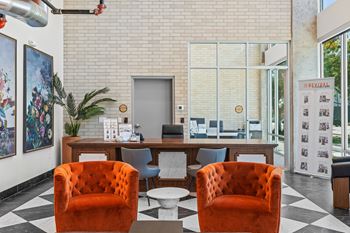 Two orange chairs are in front of a desk with a plant and pictures on the wall.